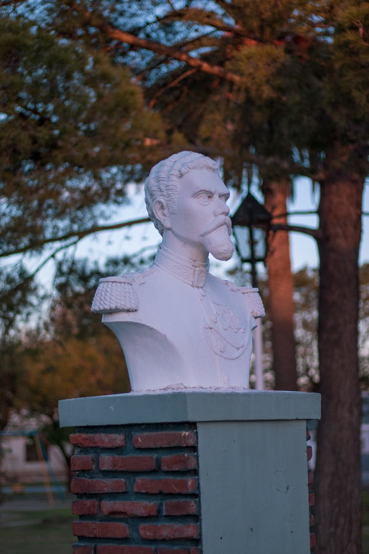 Busto blanco de prócer en una plaza al atardecer
