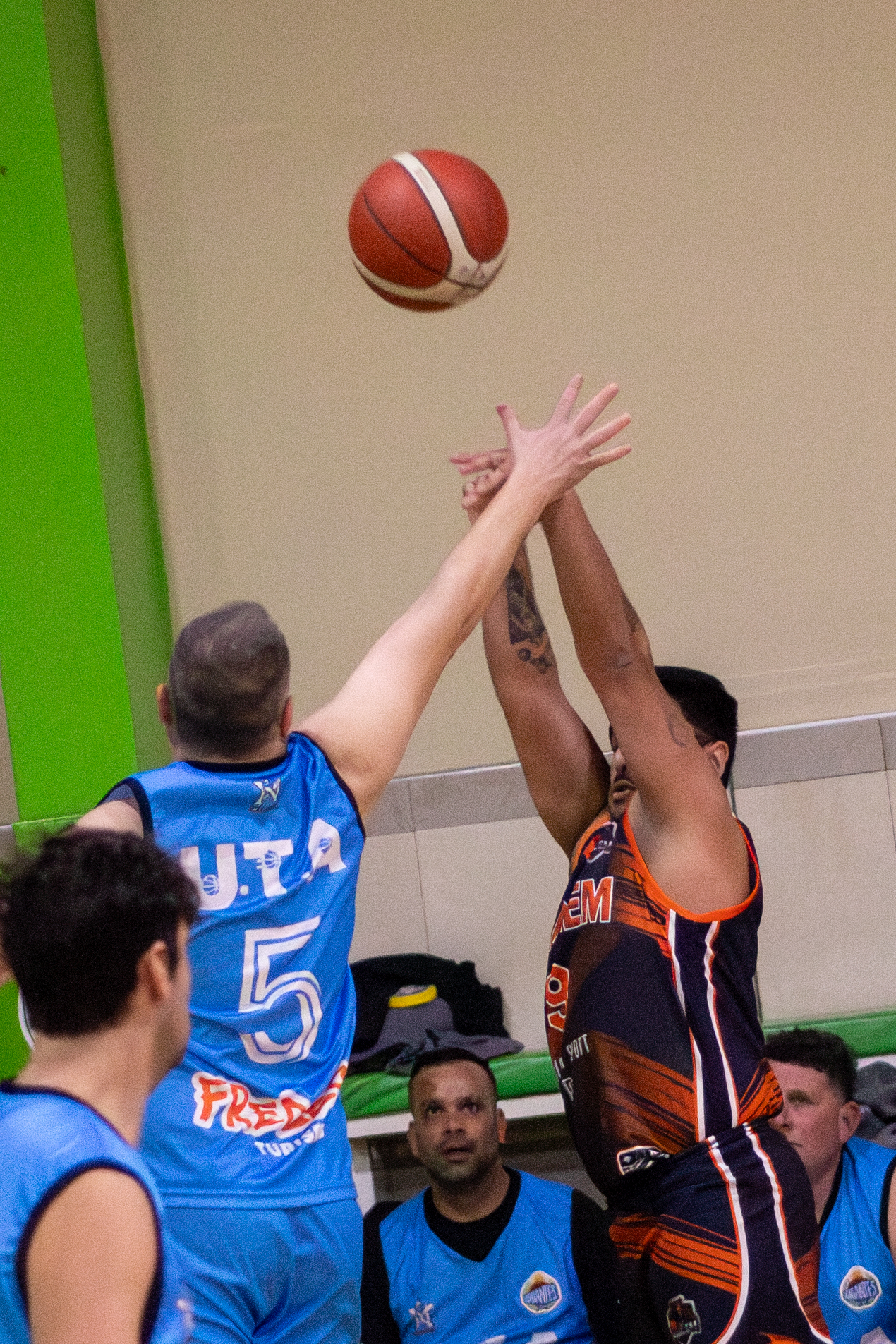 Lanzamiento de básquet con la pelota en el aire y un defensor saltando
