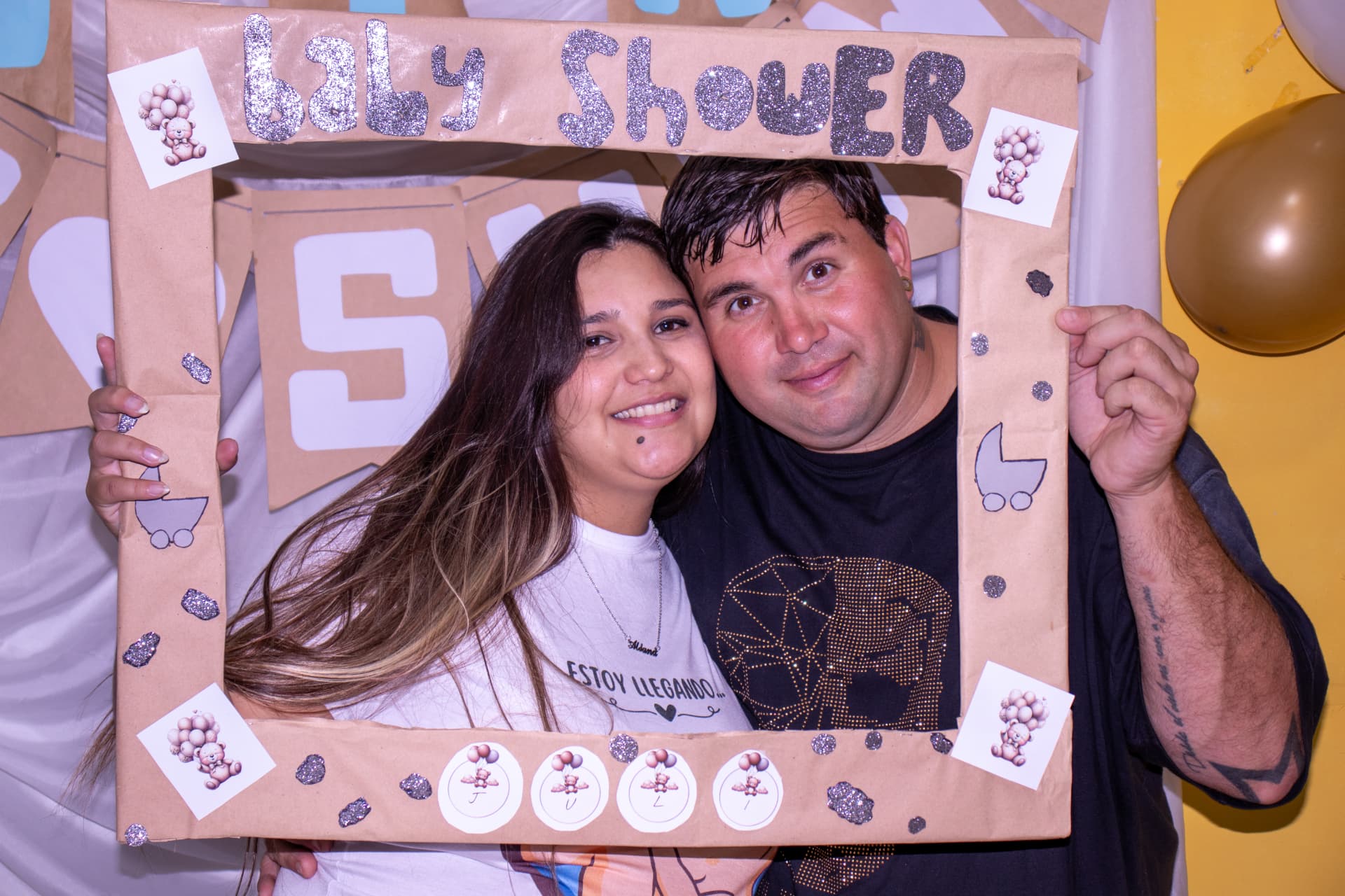 Pareja posando con un marco de baby shower en la fiesta