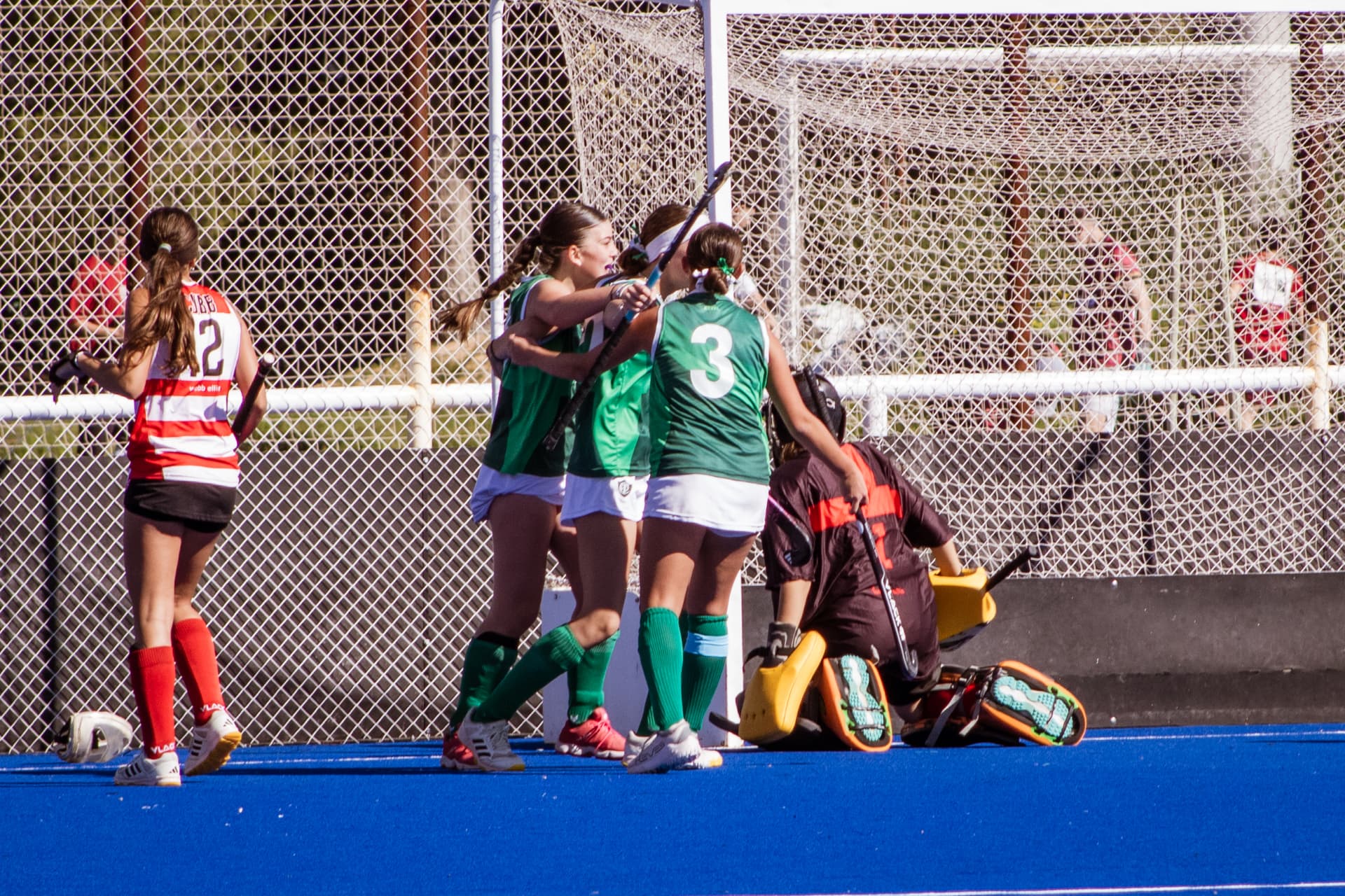 Jugadoras de hockey abrazándose para festejar un gol junto al arco