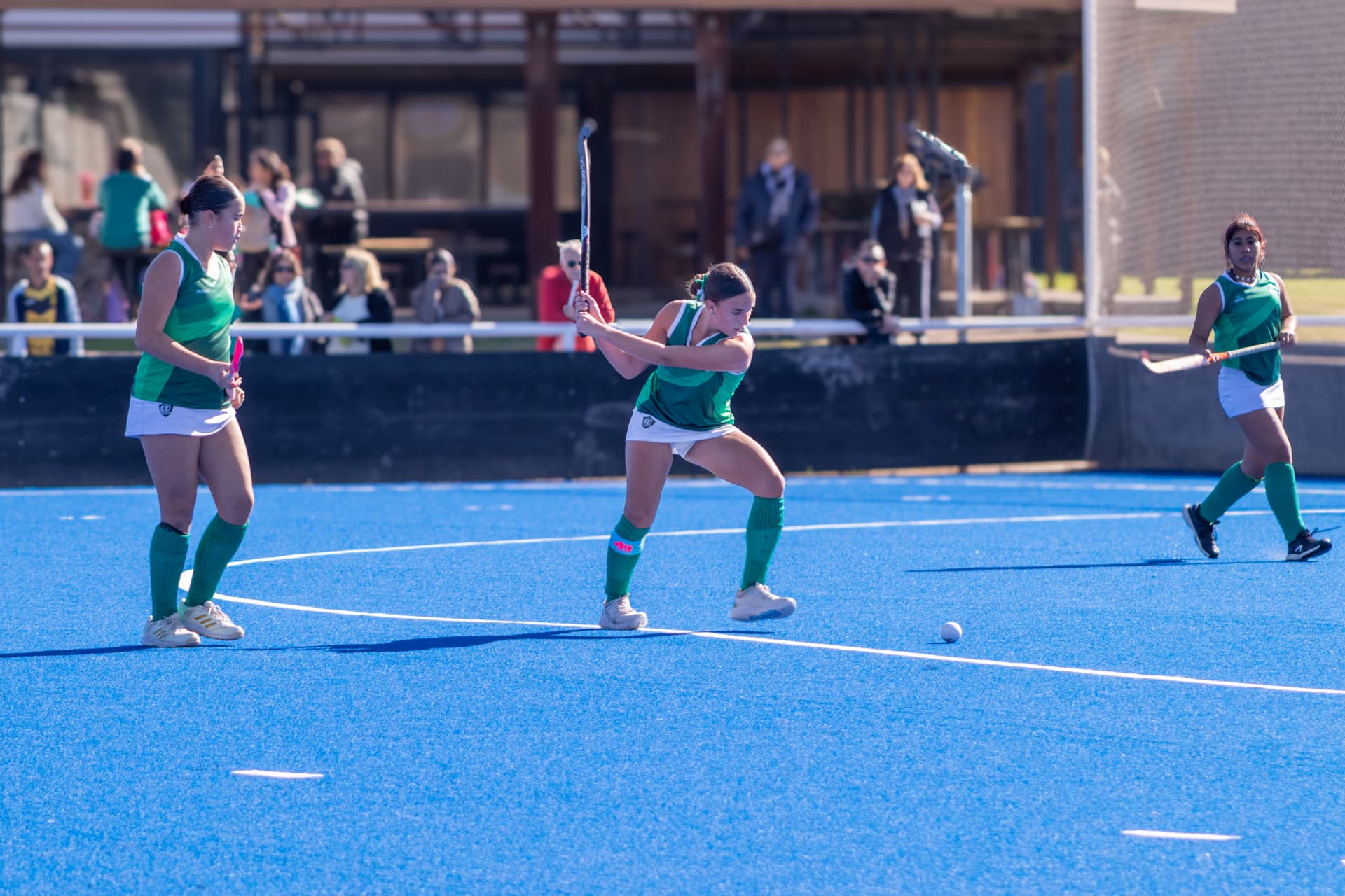 Tres jugadoras de hockey en jugada sobre cancha azul
