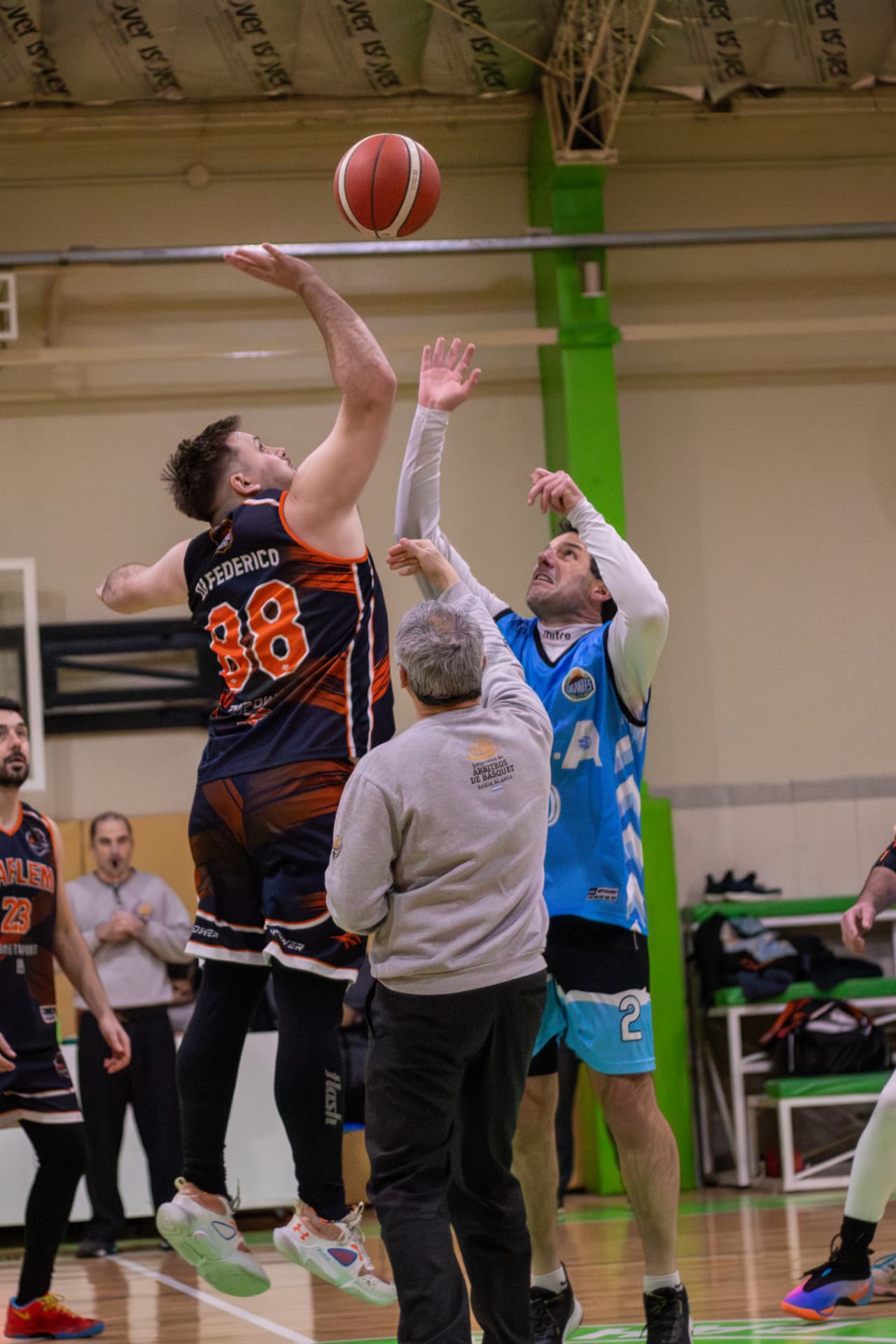 Salto inicial entre dos jugadores de básquet con el árbitro en el medio