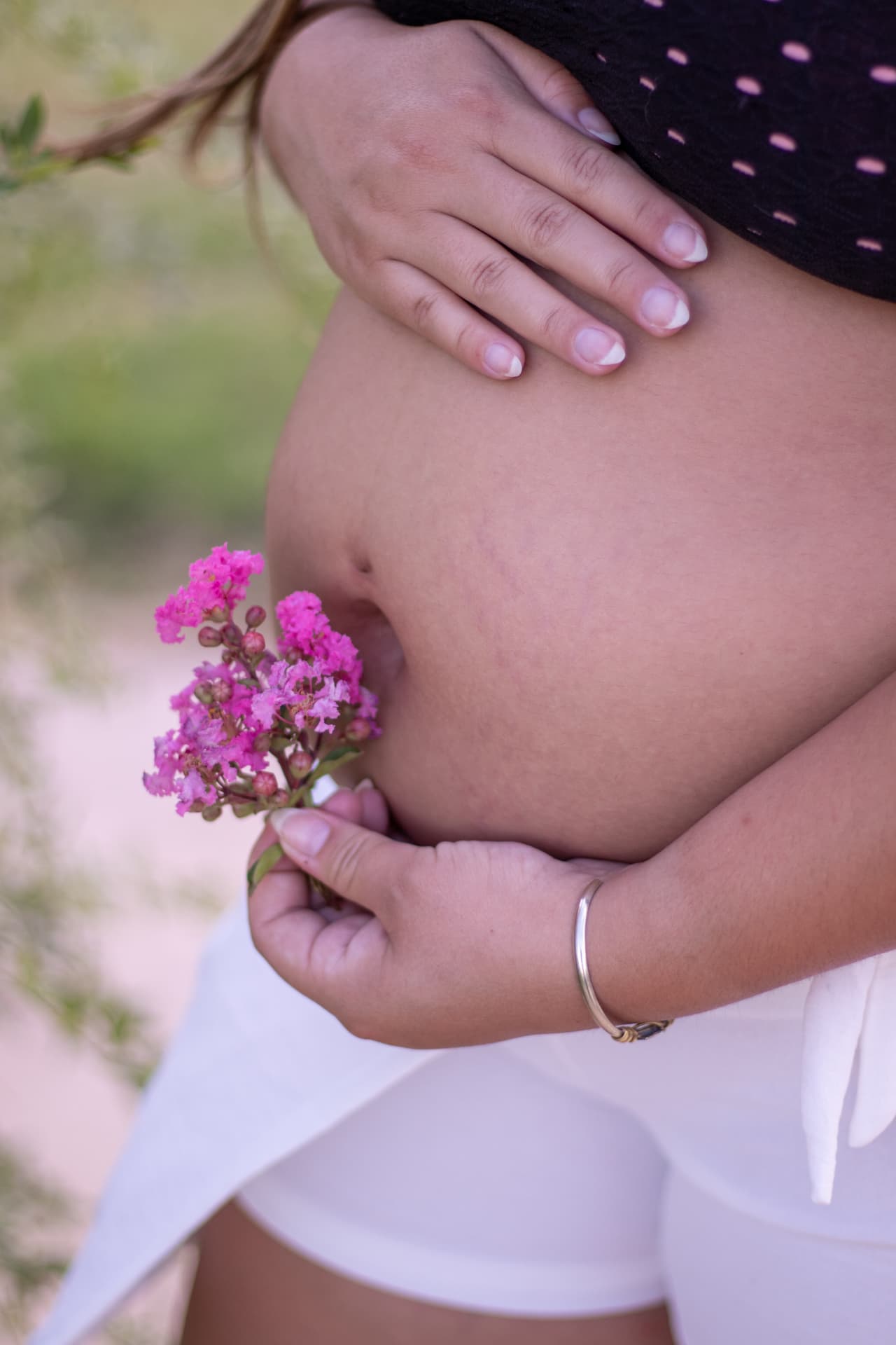 Detalle de la panza de embarazo con flores rosas en la mano